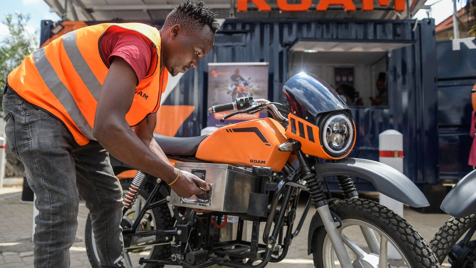 A photograph showing a man removing a battery from an orange, electric motorbike.