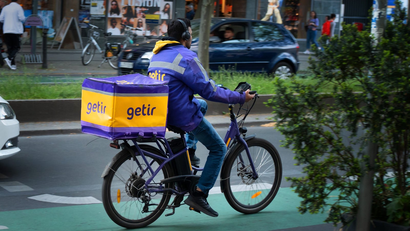 A messenger from the delivery service Getir rides an e-bike along a green bike path in a city road.