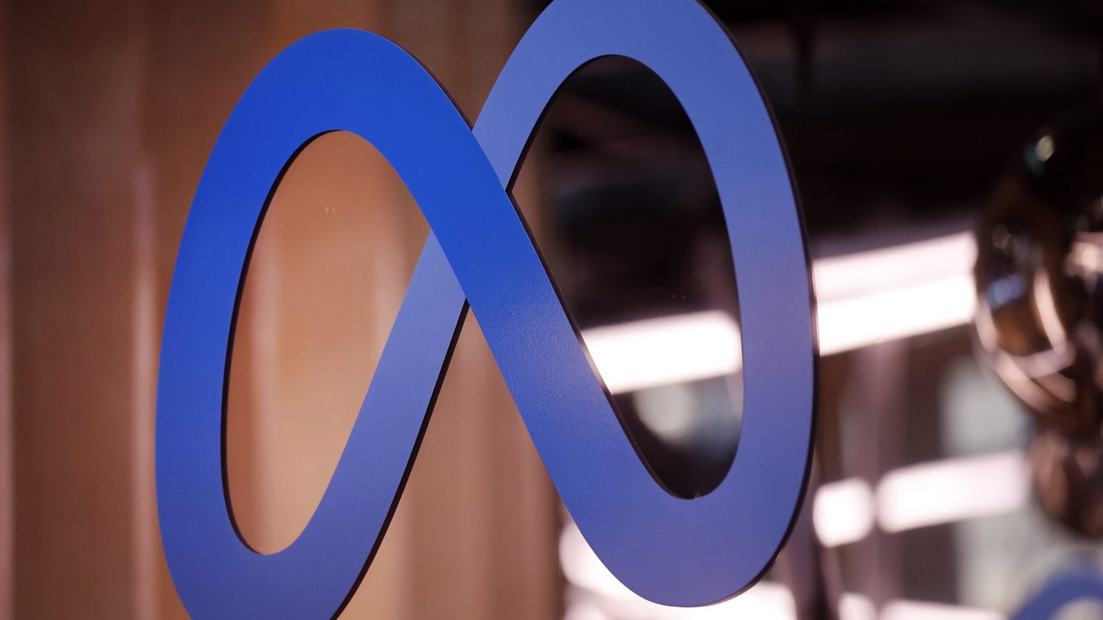 A blue infinity symbol logo representing Meta, set against a blurred background.