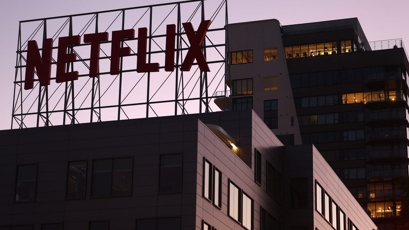 A photo of the Netflix logo displayed at the top of a building at sunset.