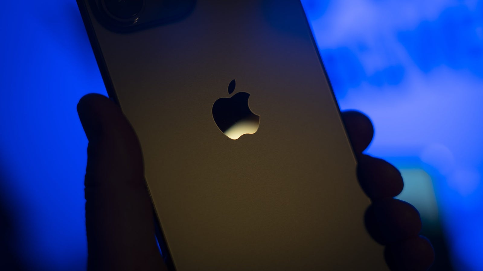 A photo showing the Apple company logo on the backside of an iPhone, held by a hand.