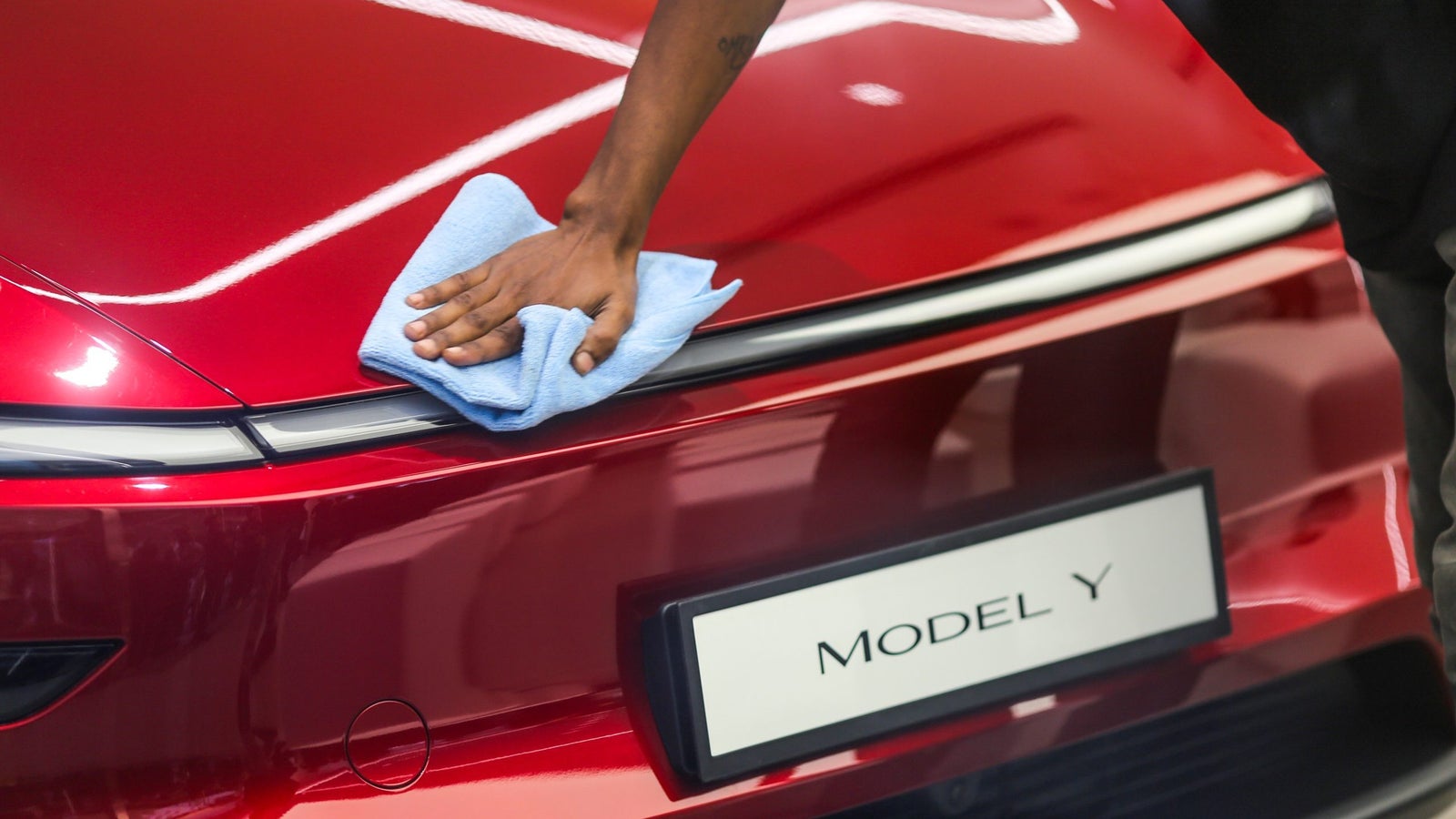 A person cleaning the rear of a red car with a blue cloth, featuring a visible 'MODEL Y' badge beneath the cleaning area.