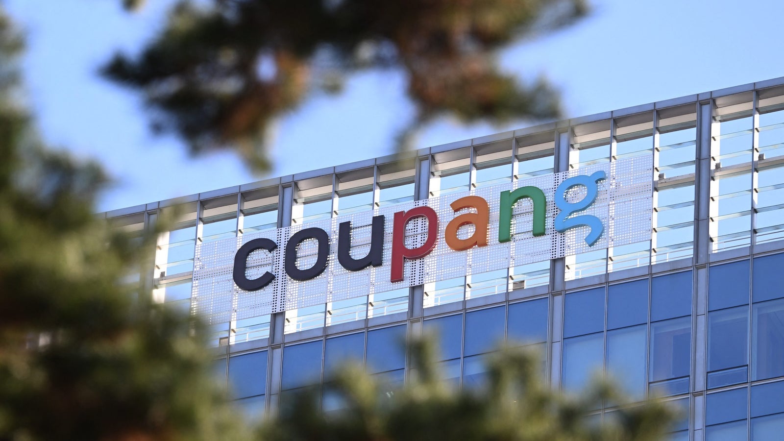 Signage of Coupang prominently displayed on a modern building, partially obscured by tree branches.