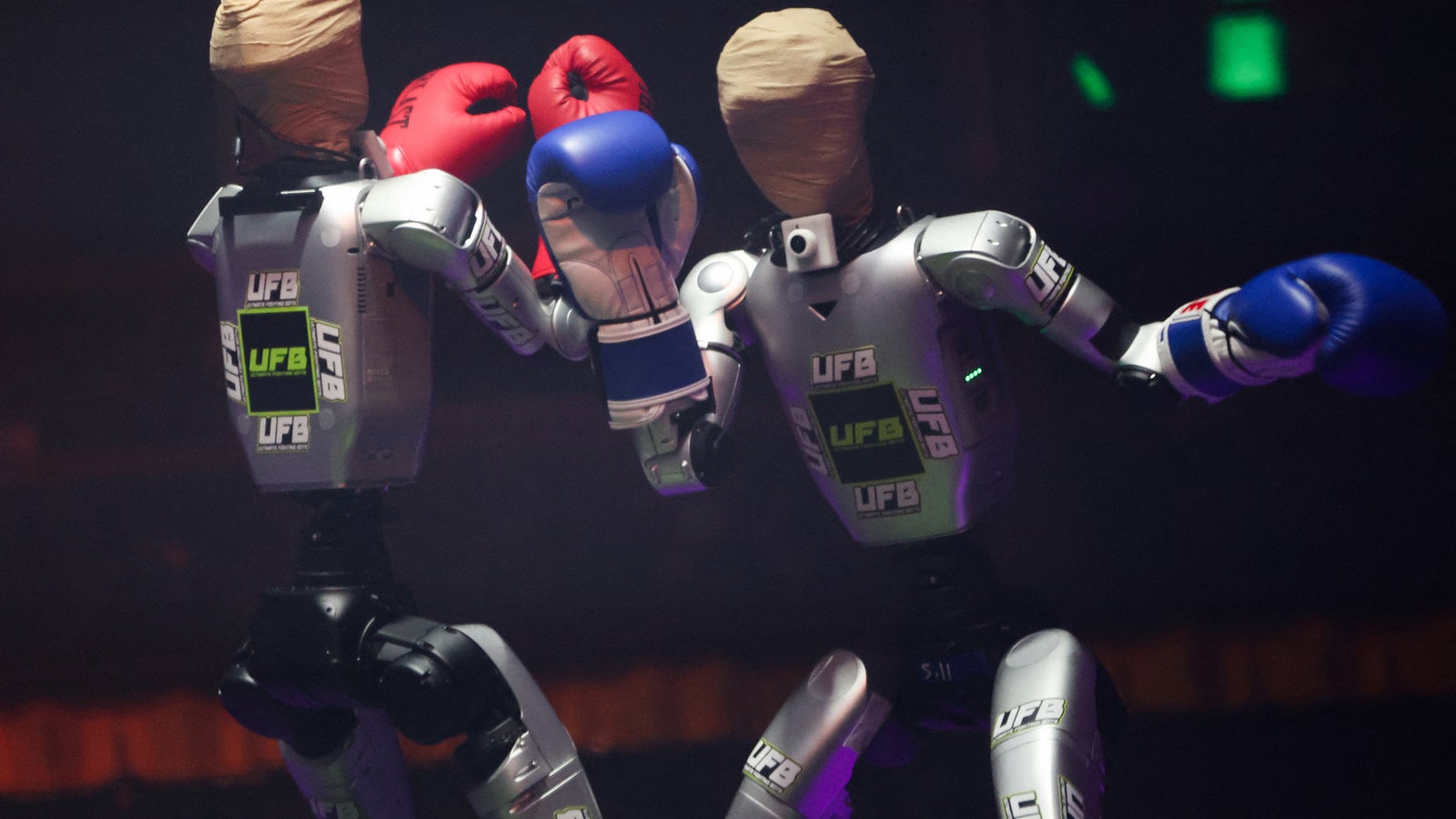 Two humanoid robot fighters with boxing gloves in a staged boxing match, featuring head coverings and UFB branding.