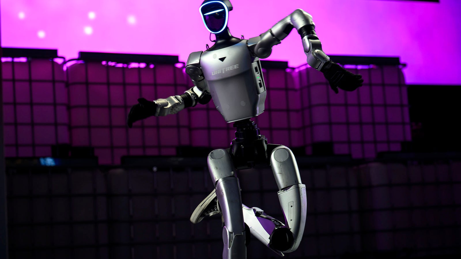A humanoid robot with a sleek silver design performing a dance move against a purple-lit background.