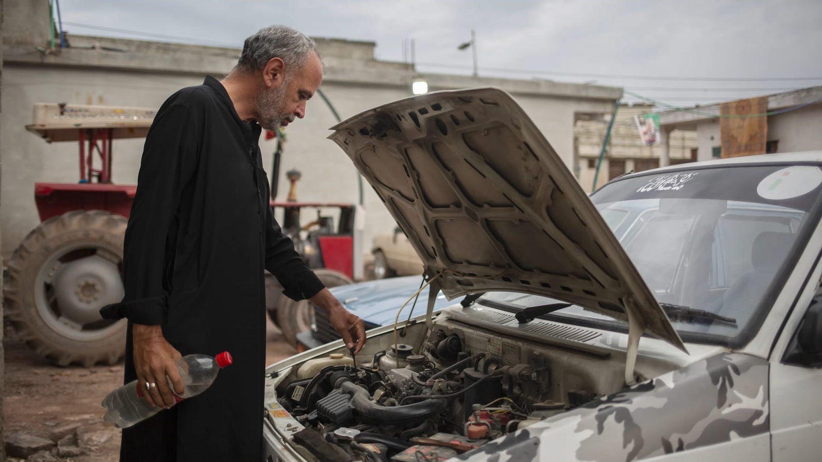 Basharat Buraak, who works as a driver for various ride-hailing apps including Careem and In-Drive checks his car and fills water in the radiator.