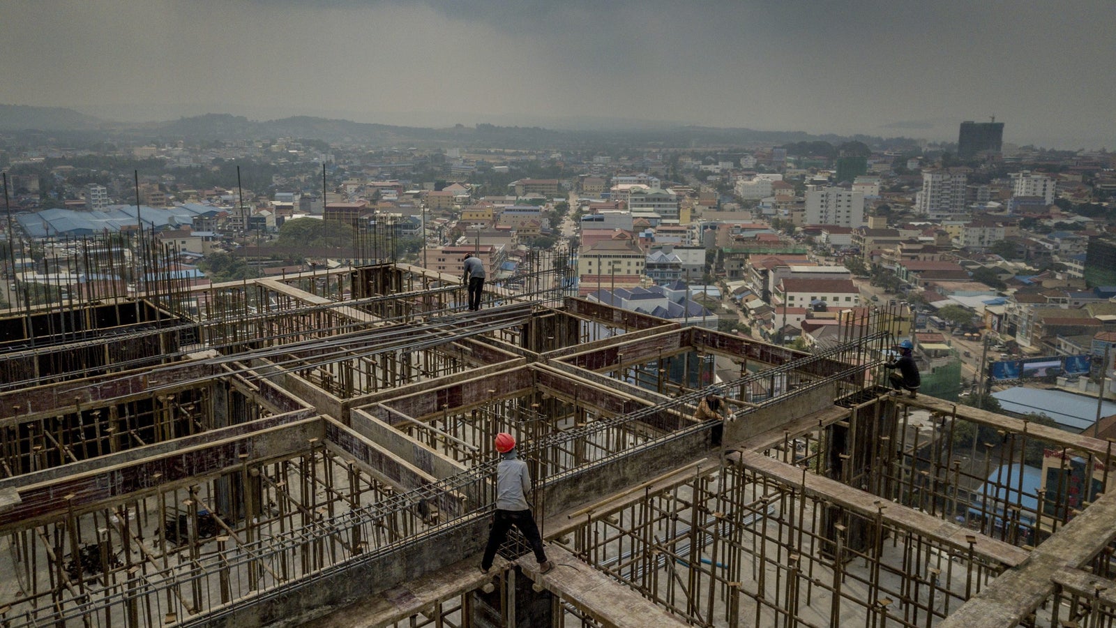 A photo showing a construction worker atop a hi-rise building being built in a city.