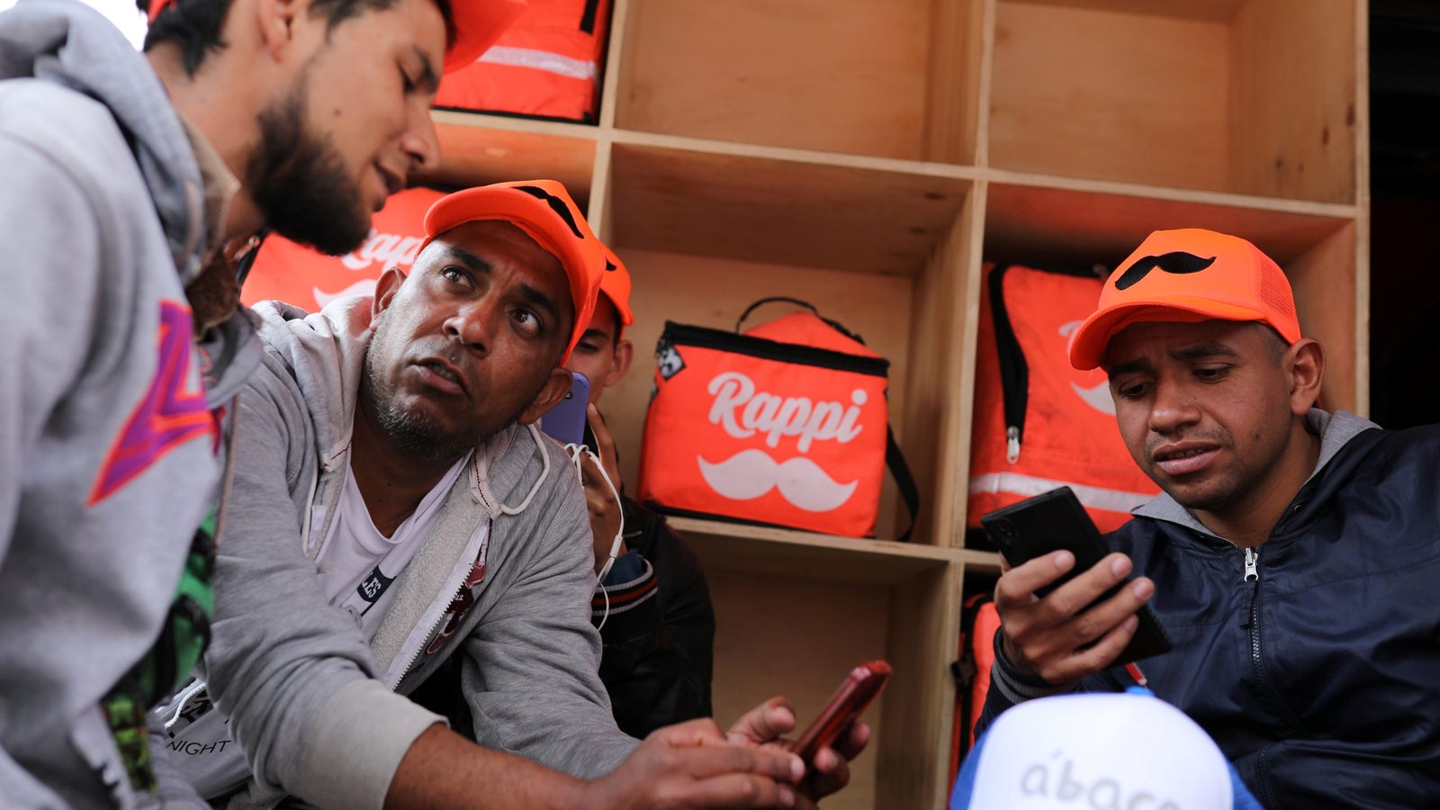 A group of Rappi delivery men are seated and using their cell phones.