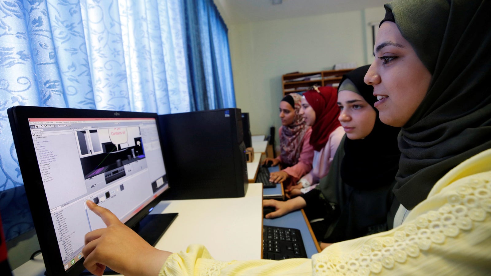 A photo showing women working on computers in a room near windows.