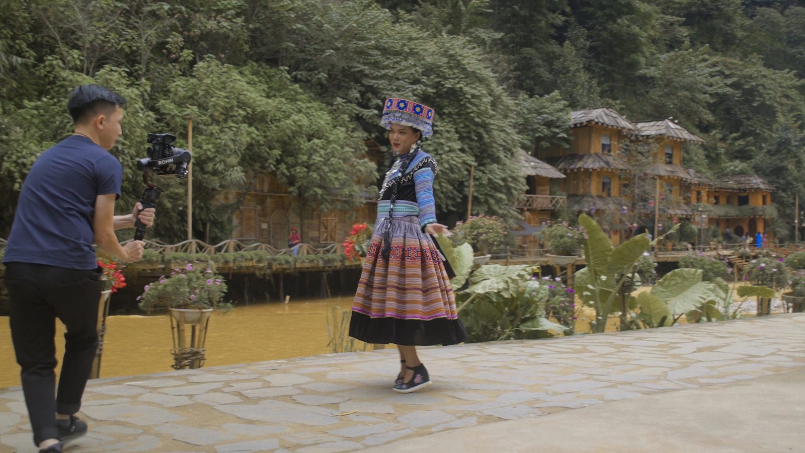 A still from a video showing a person dressed in traditional Vietnamese clothing, dancing for a camera near a stream in a jungle.