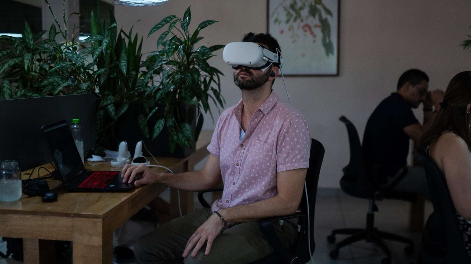 A photo showing a man wearing VR glasses at his laptop in a coworking space.