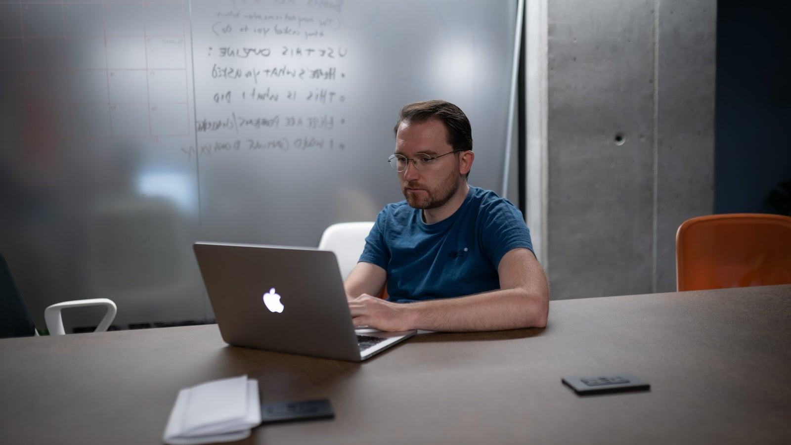 A photo of a man working on his laptop in a grey room.