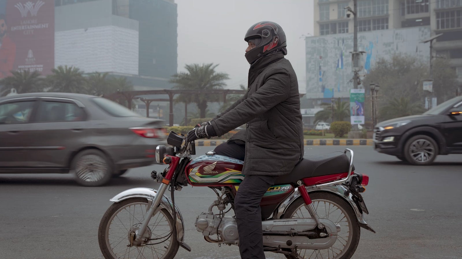 A photo of a man sitting on a motorbike on a busy street in Lahore, Pakistan.