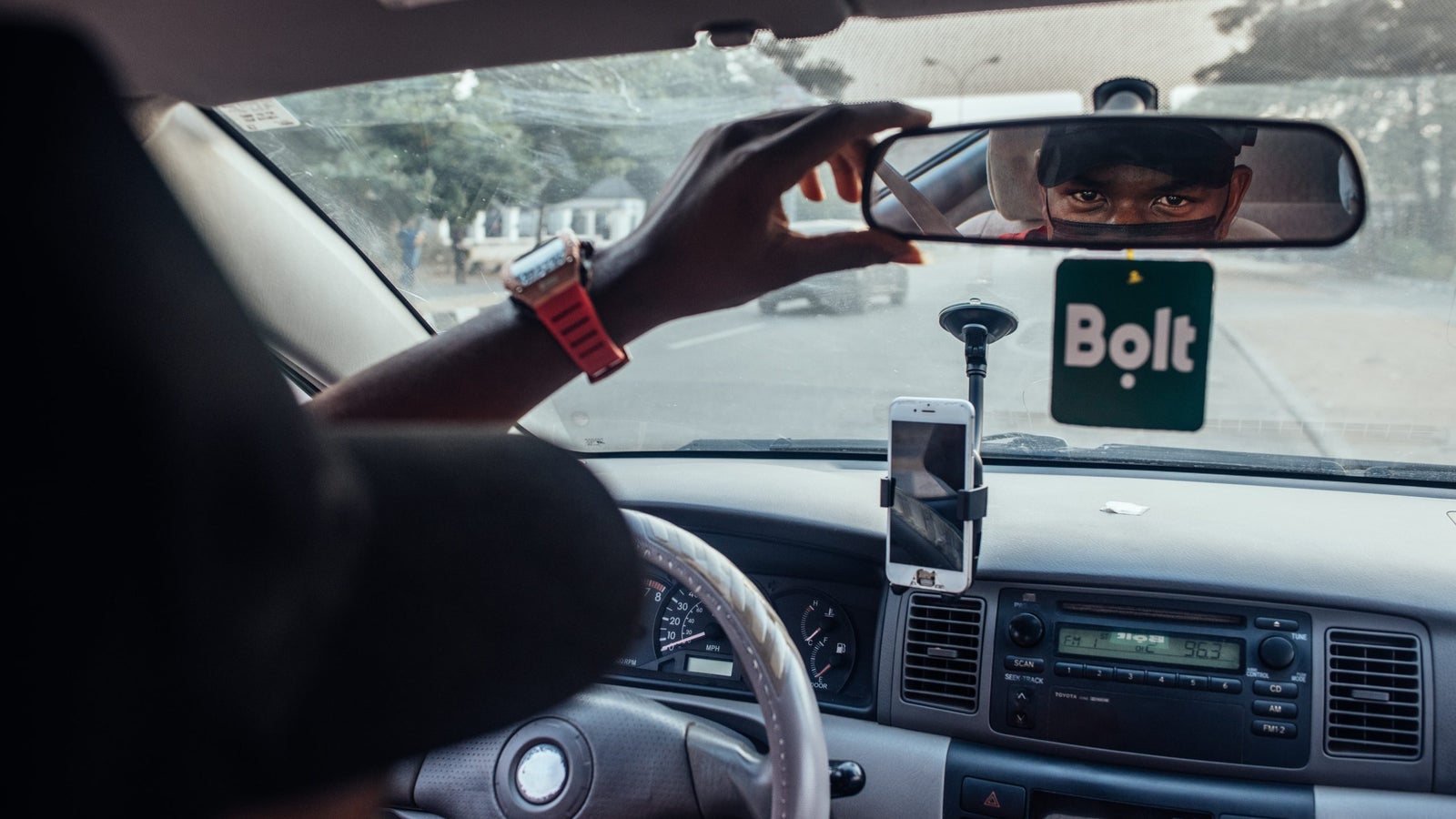 A man looks into the rearview mirror of his car, a Bolt sign hangs below it.