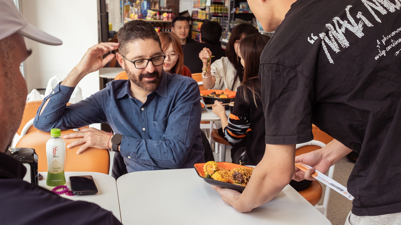 A man in a blue shirt smiles as a server brings him a plate of food in a casual dining setting.