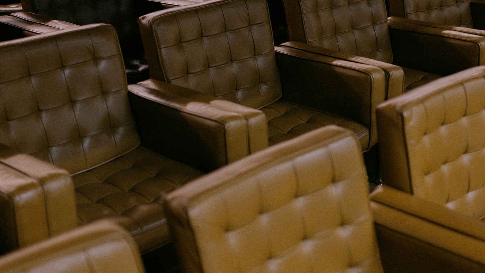 Close-up of plush, modern cinema seats arranged in rows, featuring a mix of tan and black upholstery with tufted designs, conveying a warm and inviting atmosphere.