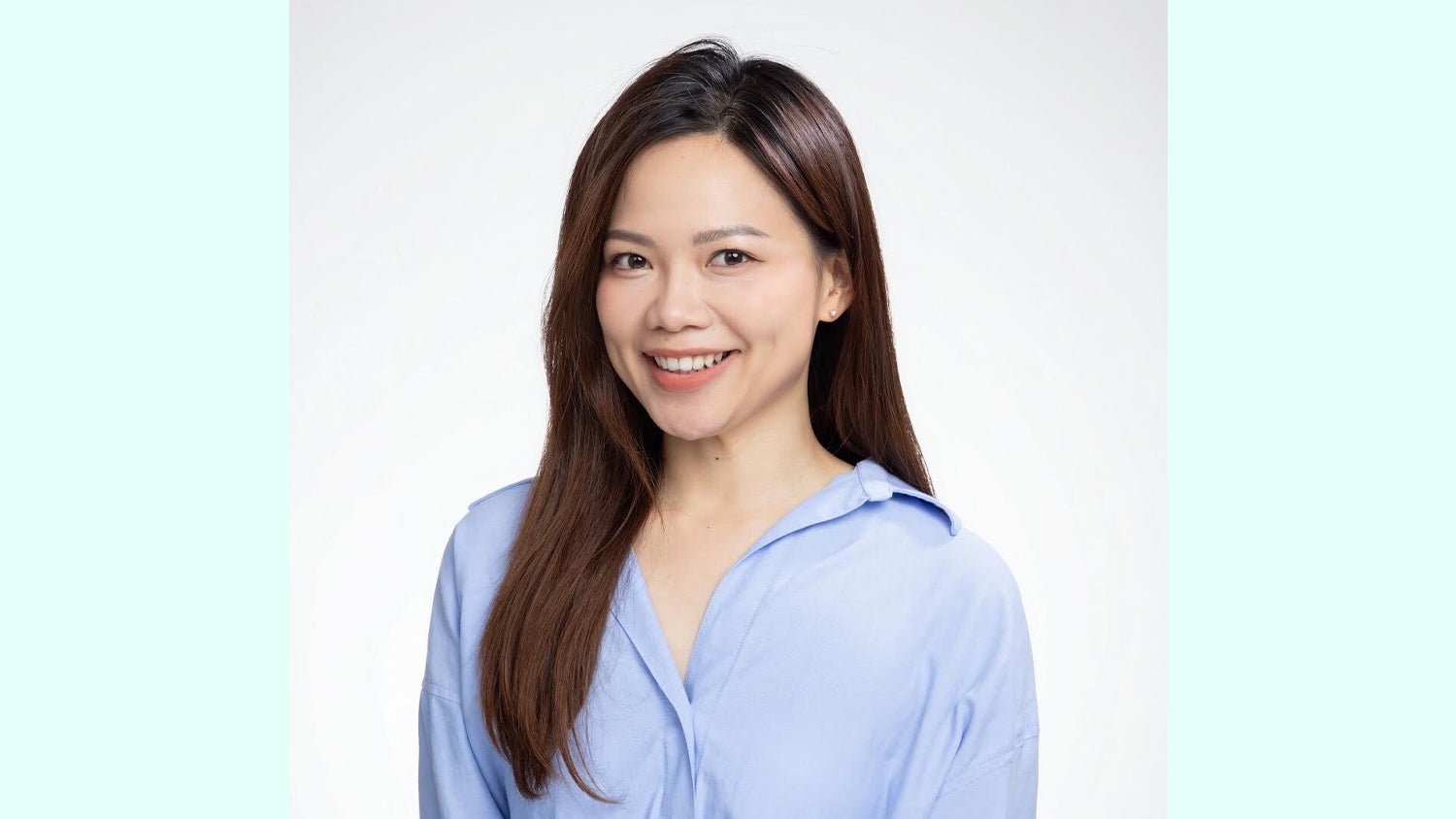 A woman with long, dark hair wearing a light blue shirt smiles at the camera against a soft white background.