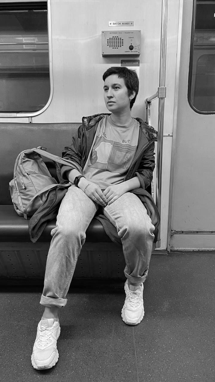 A black and white photograph showing a woman seated by herself with a backback on a subway car
