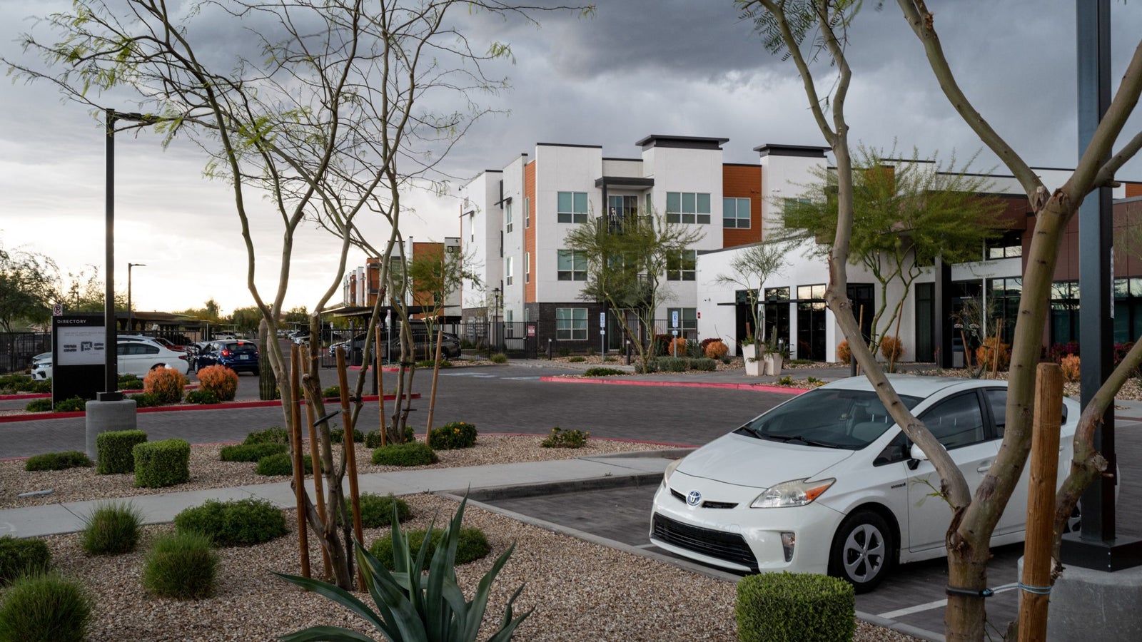 A photograph of an apartment complex with neatly landscaped desert plants and cars parked in a parking lot.